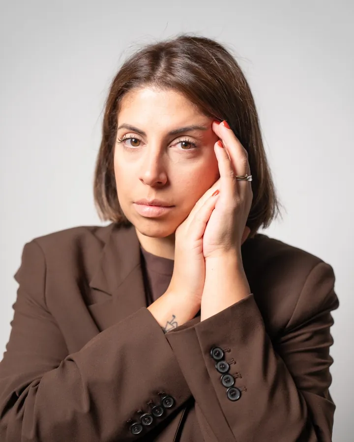 Antonella con il blazer marrone, la mano sulla guancia